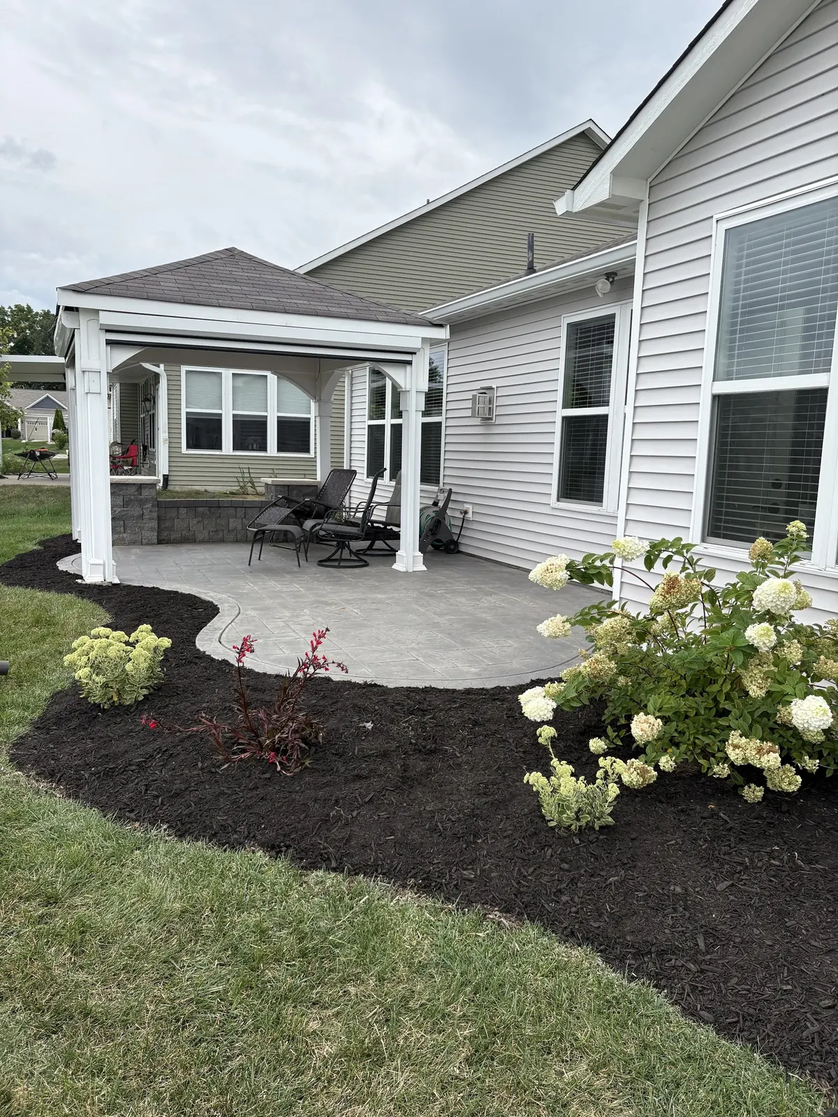 A curved bed mulched and planted with hydrangeas around a patio.