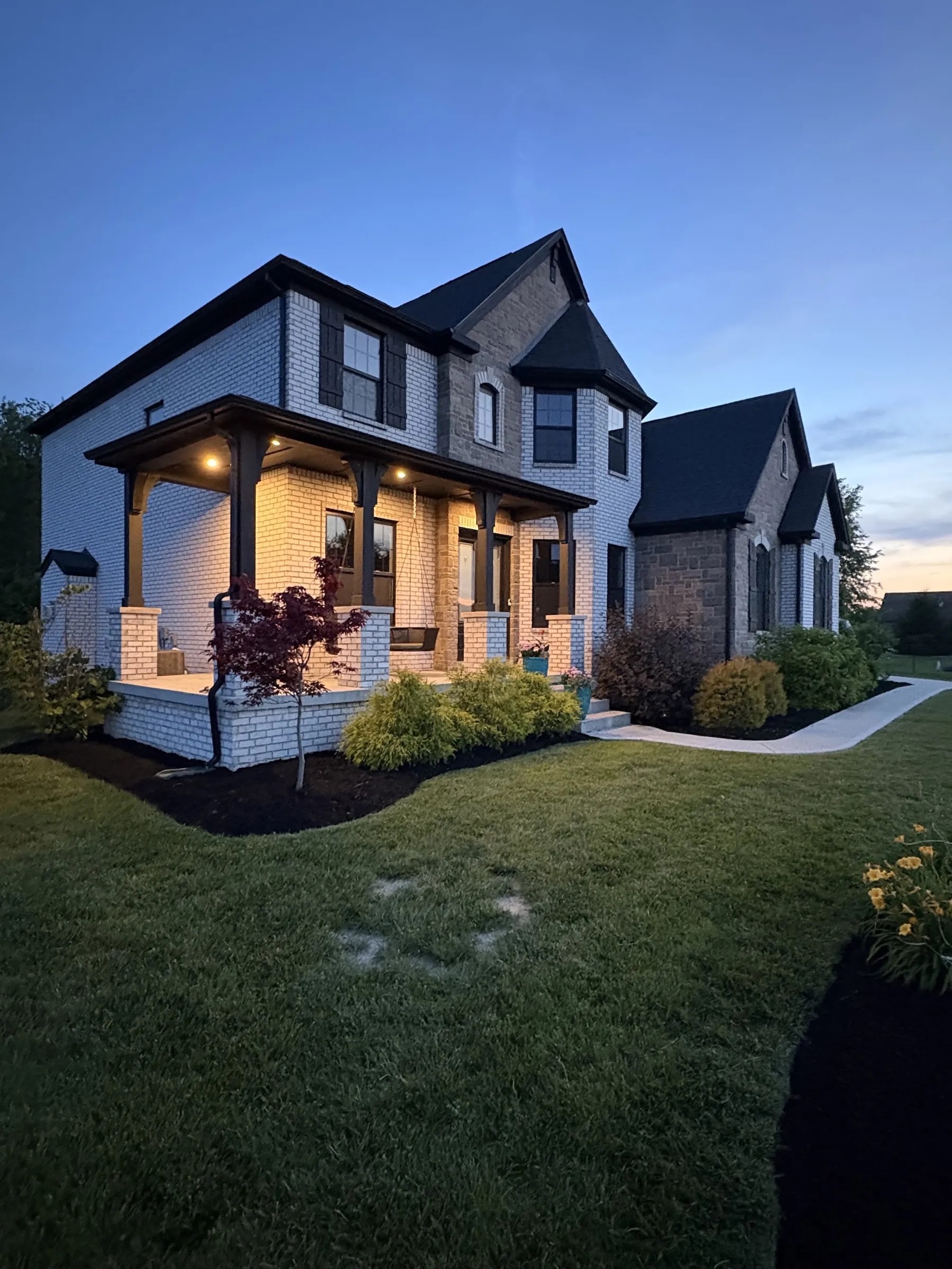 A brick house at dusk, its beds freshly mulched and the lawn cut.